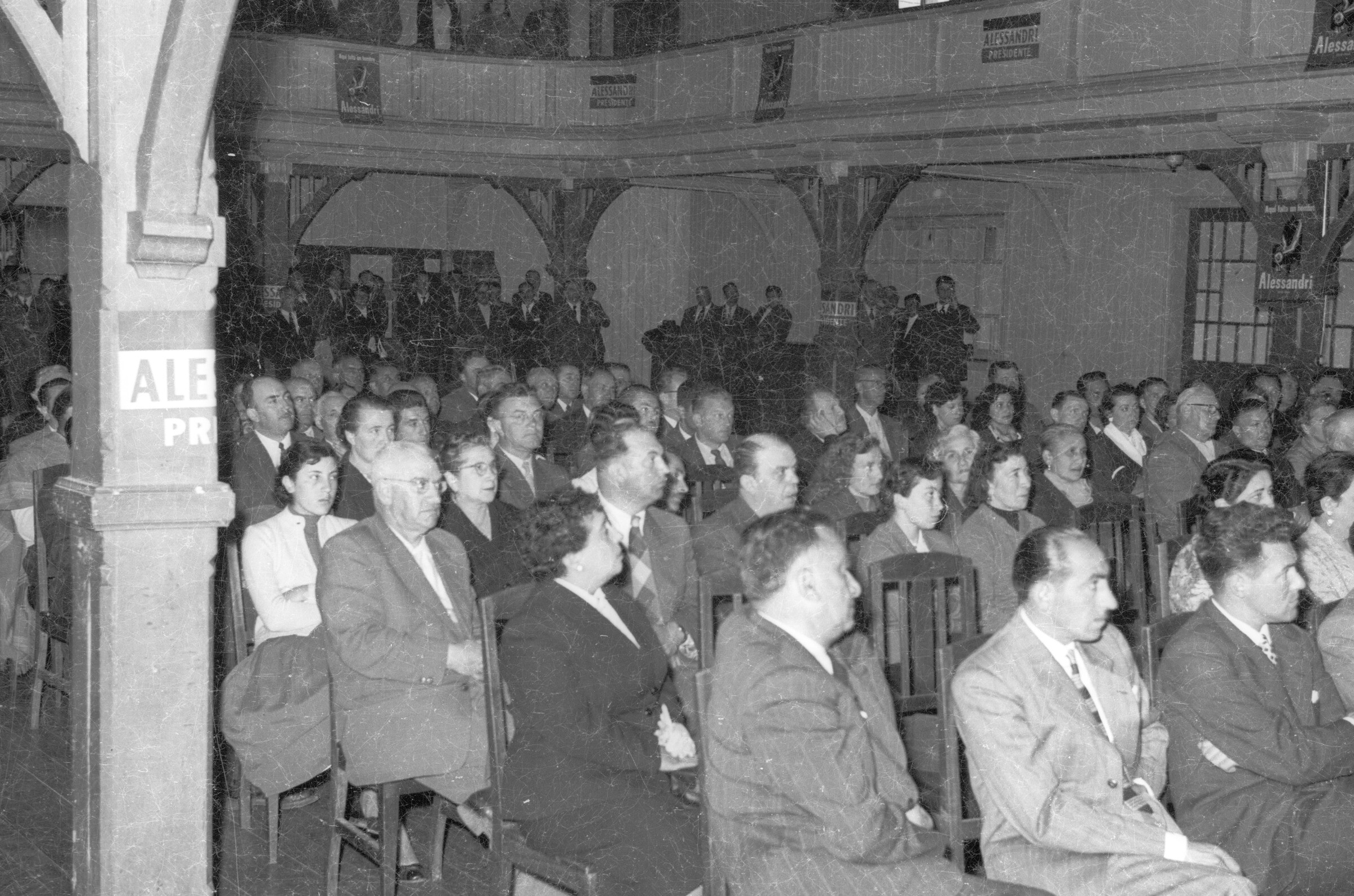 plano general de un grupo numeroso de Hombres y Mujeres sentados en sus sillas mientras escuchan el discurso de Jorge Alessandri, durante su campaña presidencial realizada en la ciudad de La Unión