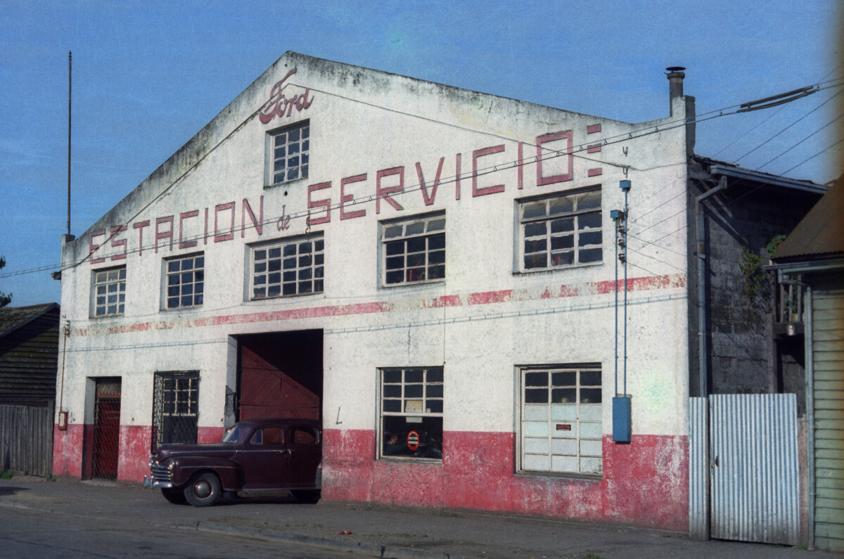 Plano general de la entrada del taller automotriz -servicio Fiat- tipo galpón, con numerosos autos y camionetas estacionados en la entrada