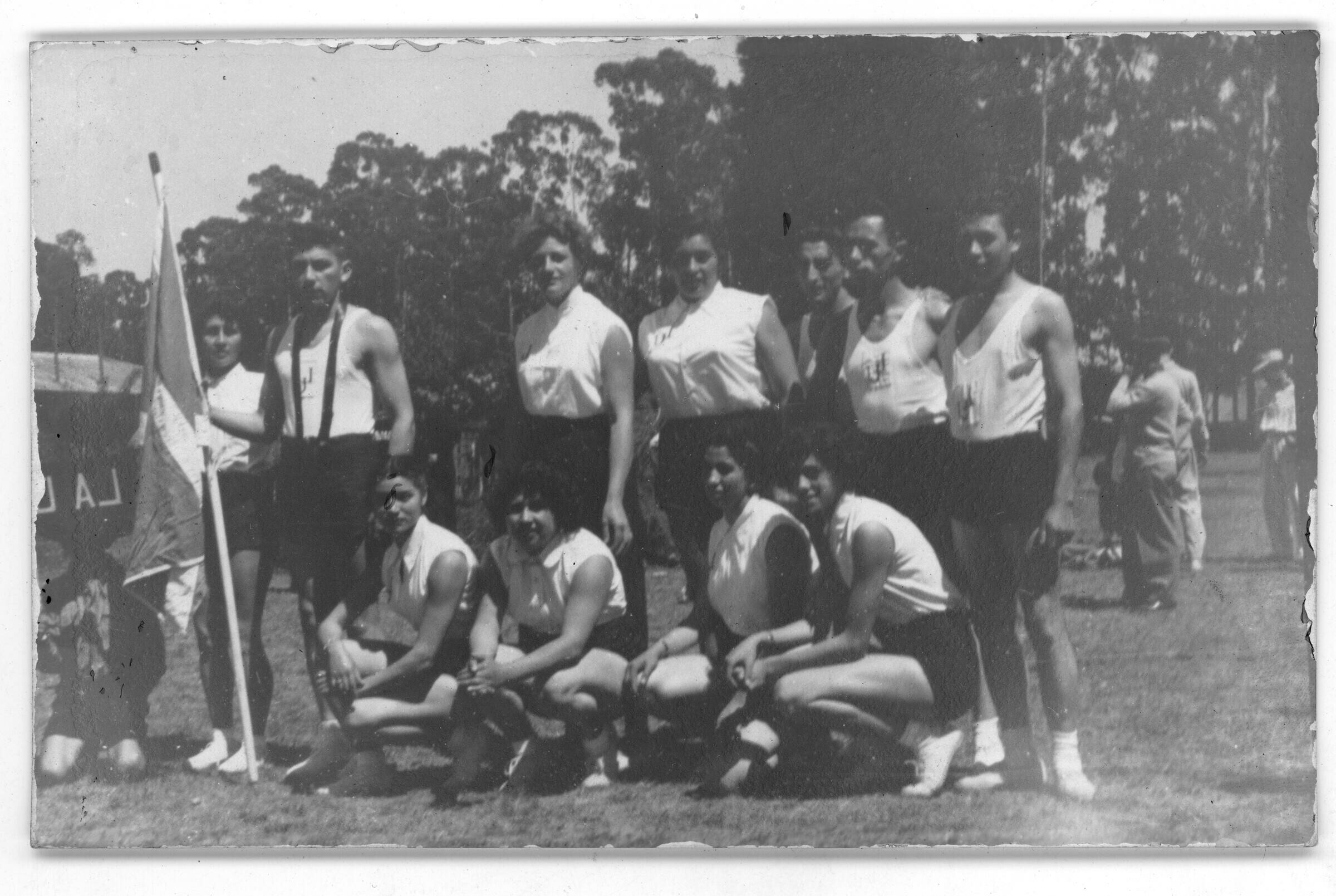 Retrato grupal de plano entero de atletas posando formados sobre la cancha. Hombres y Mujeres posan juntos en el interior de un estadio no identificado, durante un zonal sur de atletismo en tomé