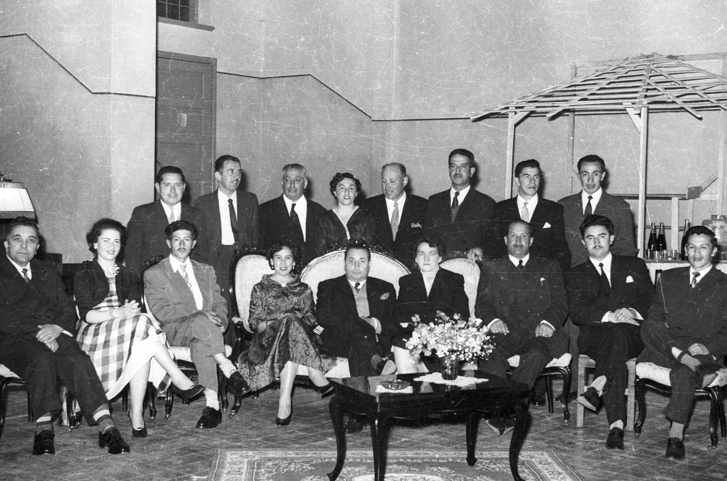 Retrato grupal de plano entero de Mujeres y Hombres posando formados en dos hileras. Todos visten formalmente ya que se encuentran en un banquete realizado en el gimnasio de la escuela superior de niñas Nº3
