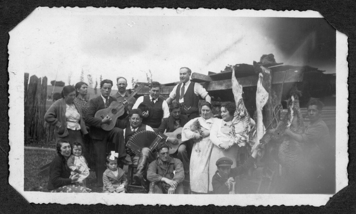 Retrato grupal de personas en una celebración. Hay hombres adultos, mujeres adultas, niños y niñas. Algunas personas tienen instrumentos como guitarras y un acordeón, y algunas personas tienen animales carneados.