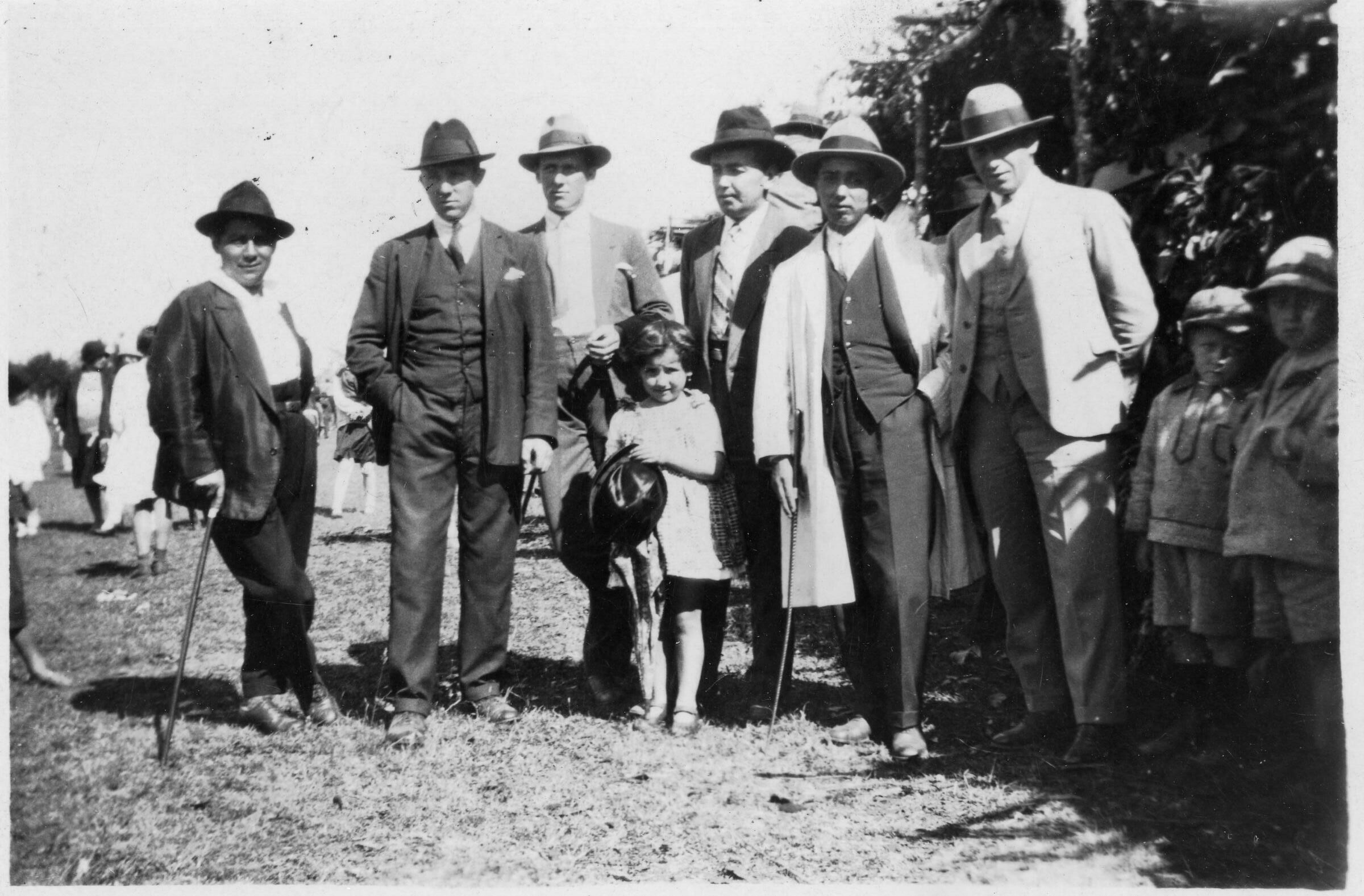 Retrato grupal de plano entero de un hombres vestidos de Traje y una niña posando parados sobre el pasto en un lugar no identificado