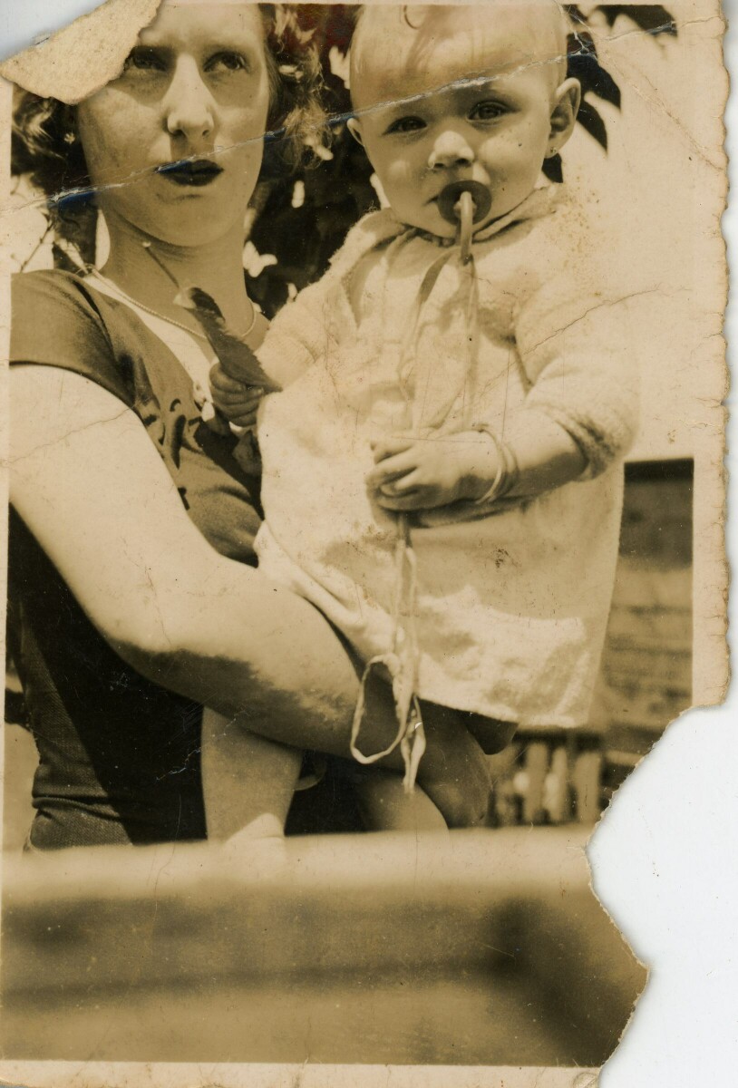 Retrato de plano medio largo  de una mujer posando con una Niña en brazos. La Niña tiene un chupete en la boca, una hoja en la mano y está mirando a la cámara.