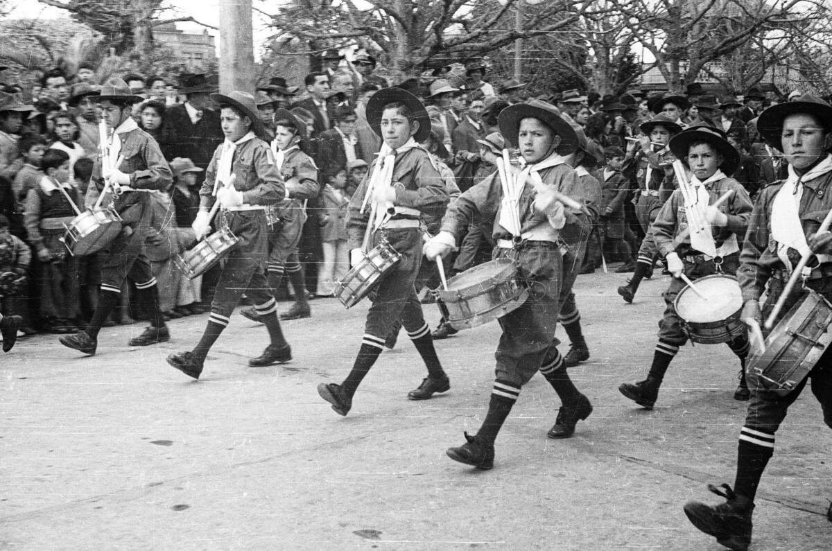 plano general de un grupo de Niños formados en hilera, pertenecientes a la banda de su colegio tocando sus instrumentos durante un desfile, a su alrededor hay un grupo de Niños, Mujeres y Hombres observándolos en un costado de la Plaza de la Concordia en la Unión