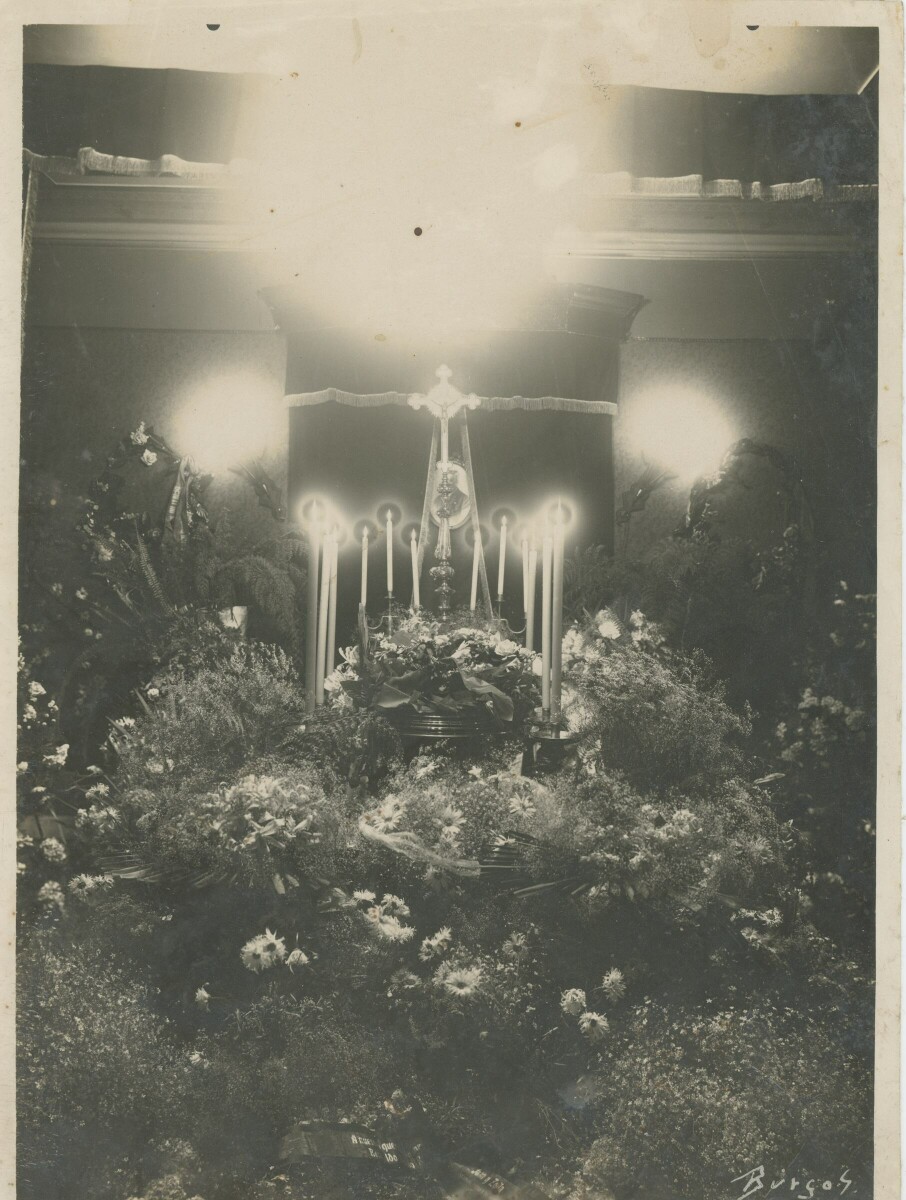 Plano general de un ataúd en un altar decorado con coronas de flores y velas durante su velorio. Lugar no identificado