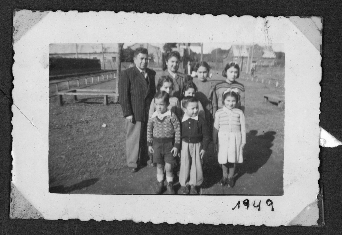 Retrato grupal de un hombre adulto, una mujer adulta, niñas y niños en entorno rural. detrás, cercas de madera y edificaciones
