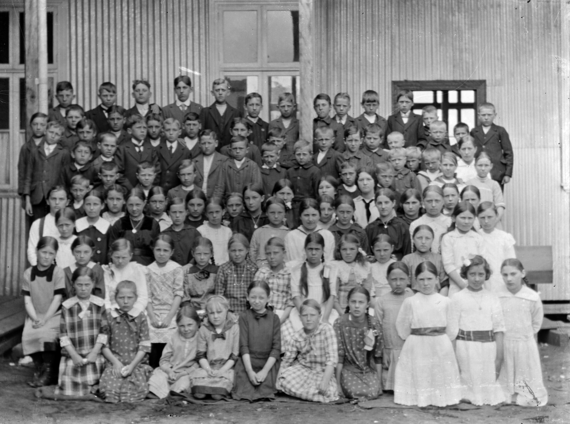 Plano general de un grupo de niños y niñas posando en la entrada de un edificio de madera y lata