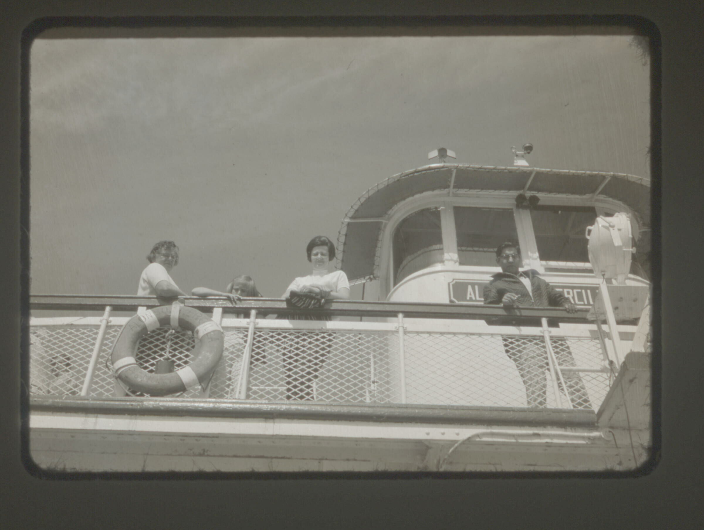 Retrato de plano entero de dos mujeres y una niña, apoyadas de la baranda de un barco. Imagen capturada desde el piso de abajo