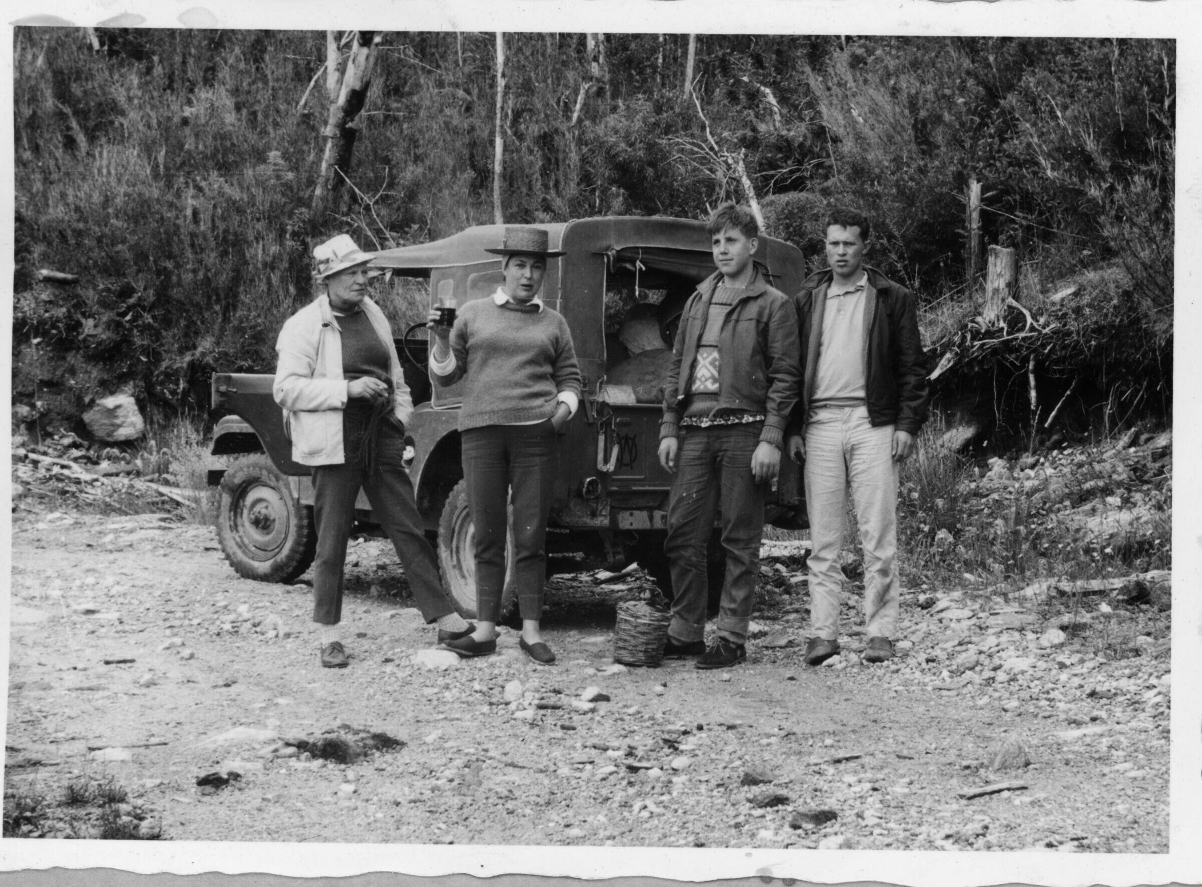 Plano entero de dos mujeres y dos hombres jóvenes, parados junto a una camioneta, la cual está estacionada al lado del camino. La primera mujer de izquierda a derecha es Olga Boettcher y está posando con un cigarro en la mano. Se encuentran de paseo camino a Corral