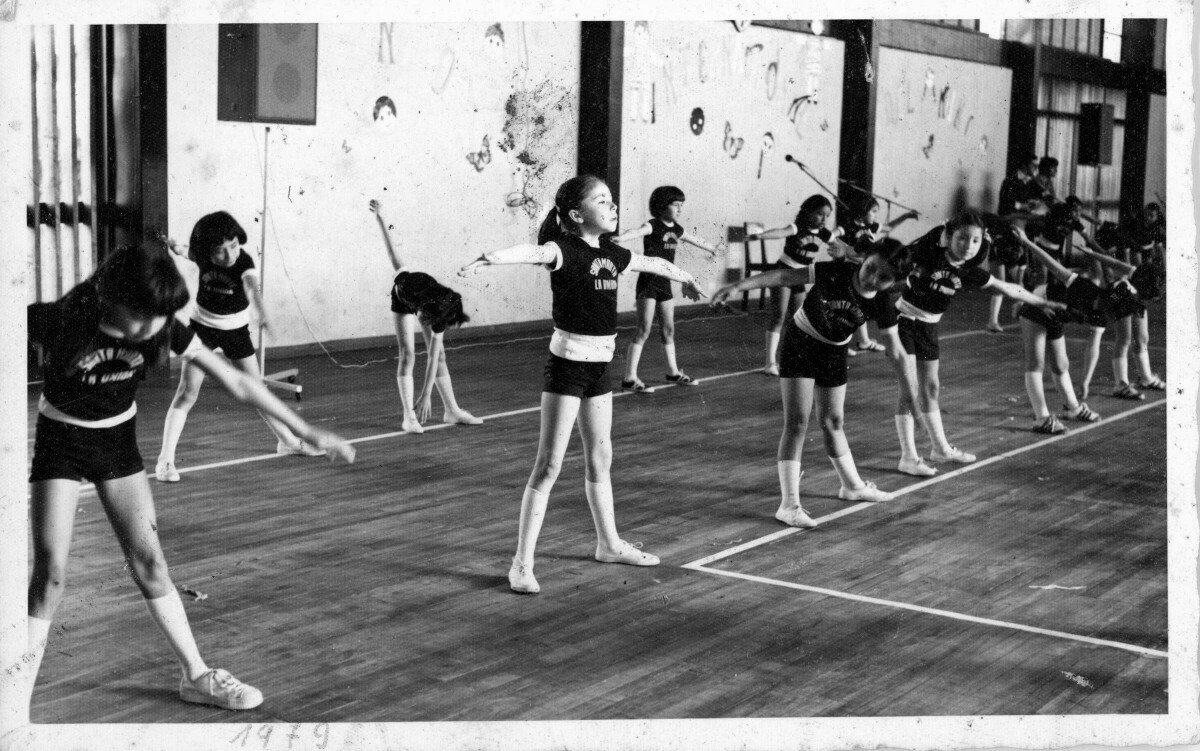 Plano general de un grupo de niñas, realizando ejercicios aeróbicos en el marco de una revista de gimnasia del colegio Santa Marta en el Gimnasio Fiscal