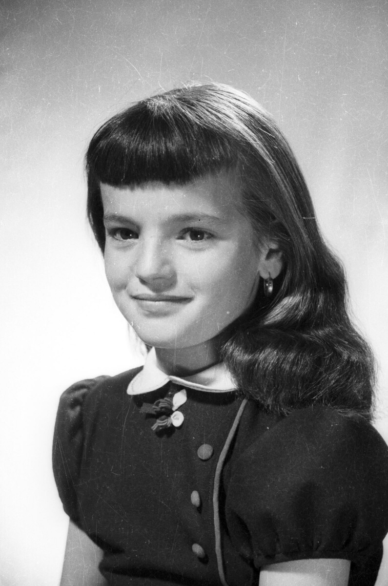Retrato de estudio de una niña sonriendo mientras posa de Medio perfil. Lleva puesto un Vestido y usa chasquilla