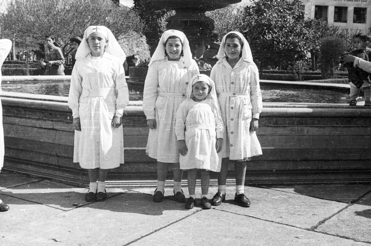 Retrato de plano entero de cuatro niñas pertenecientes a la Cruz Roja Juvenil de la Escuela Nº2 posando vestidas de blanco con una túnica sobre sus cabezas junto a la pileta ubicada en el interior de la plaza de La Concordia de La Unión