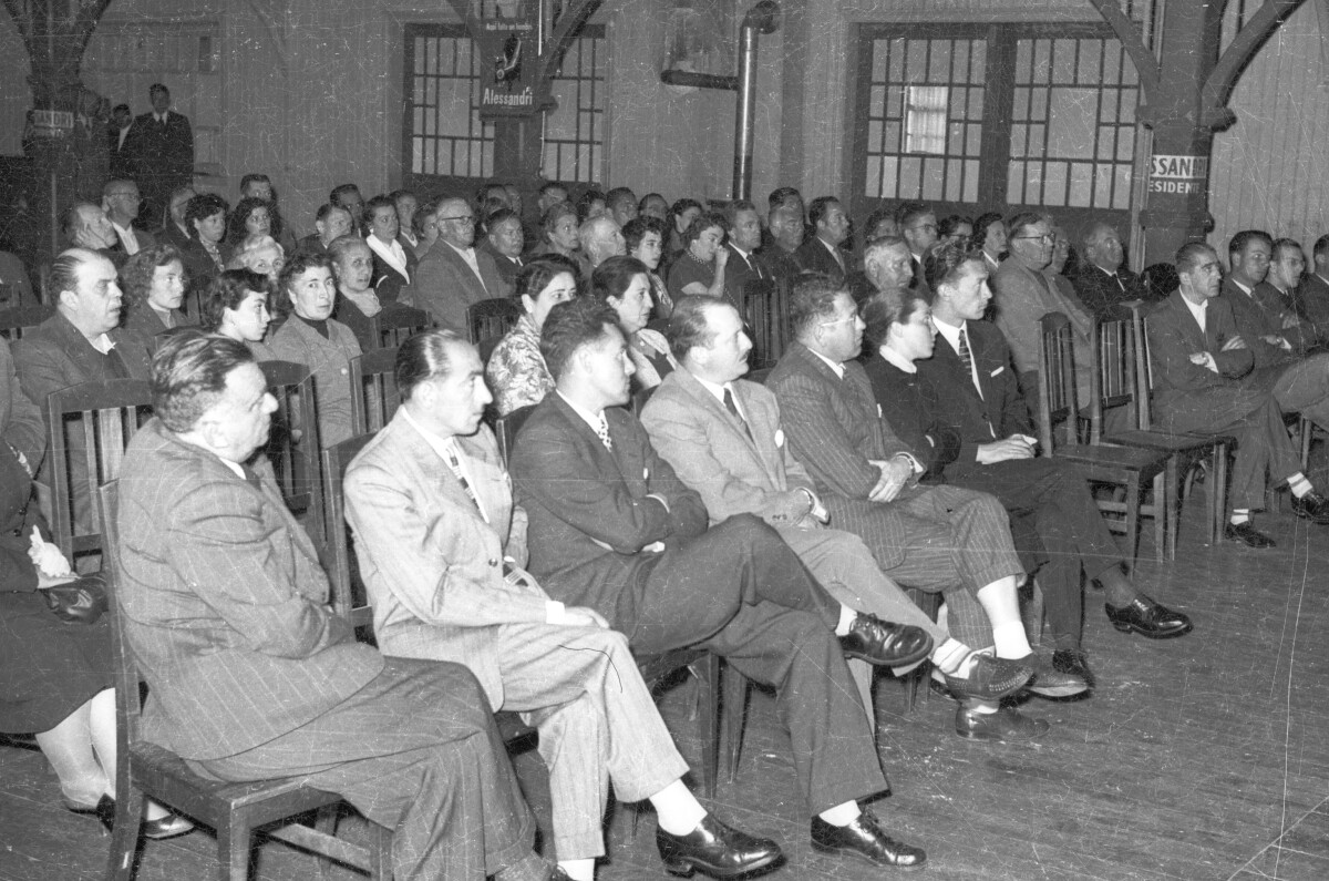 plano general de un grupo numeroso de Hombres y Mujeres sentados en sus sillas mientras escuchan el discurso de Jorge Alessandri, durante su campaña presidencial realizada en la ciudad de La Unión