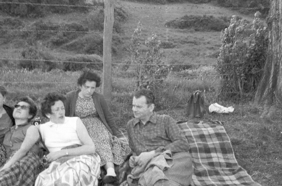 Plano entero de Gonzalo Carrasco, sentado junto a un grupo de mujeres sobre una manta, durante un paseo realizado a un Río no identificado