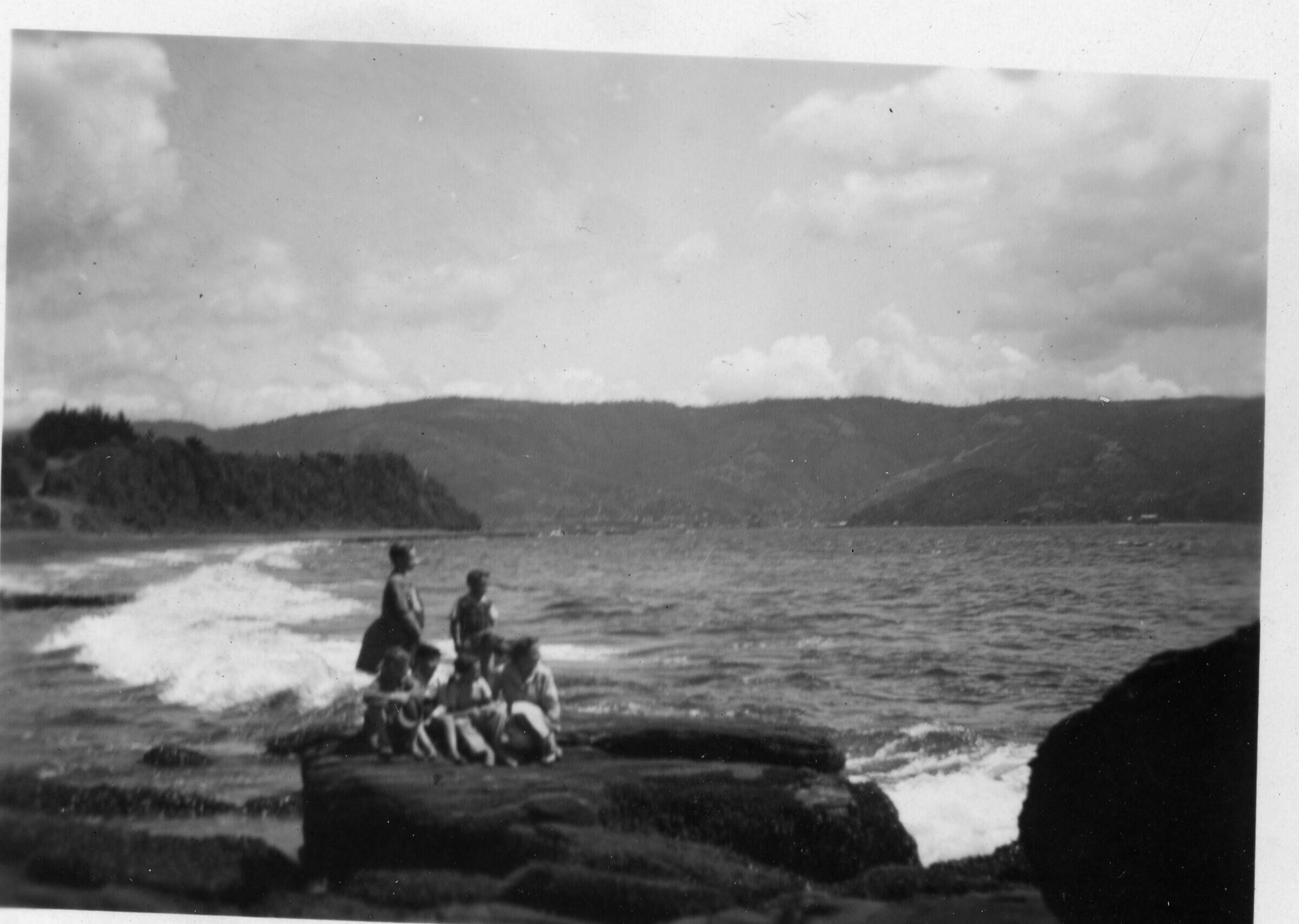 plano general de dos mujeres y un grupo de niños, reunidos sobre una roca mirando hacia el mar, durante un paseo familiar realizado a Niebla, Valdivia