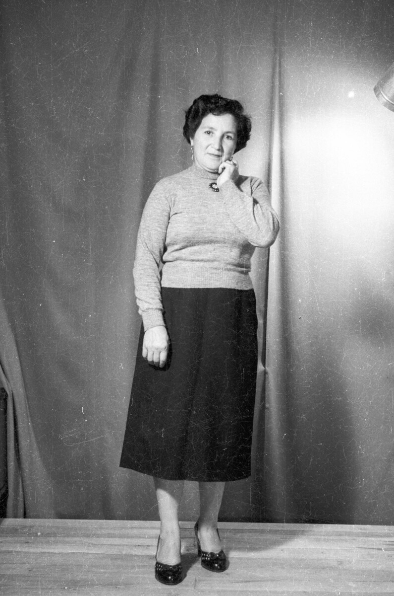 Retrato de estudio de Plano entero de una mujer mayor posando parada mientras con una mano se toca la mejilla