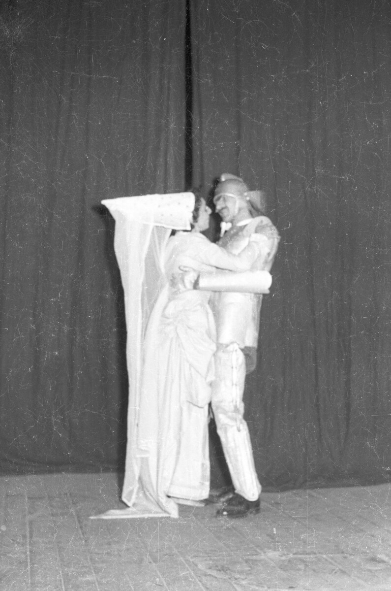 Plano entero de una doncella y un caballero medieval a prontas de darse un beso. Ambos están caracterizados para la obra de teatro que están actuando sobre la tarima del gimnasio de la escuela superior de niñas Nº2