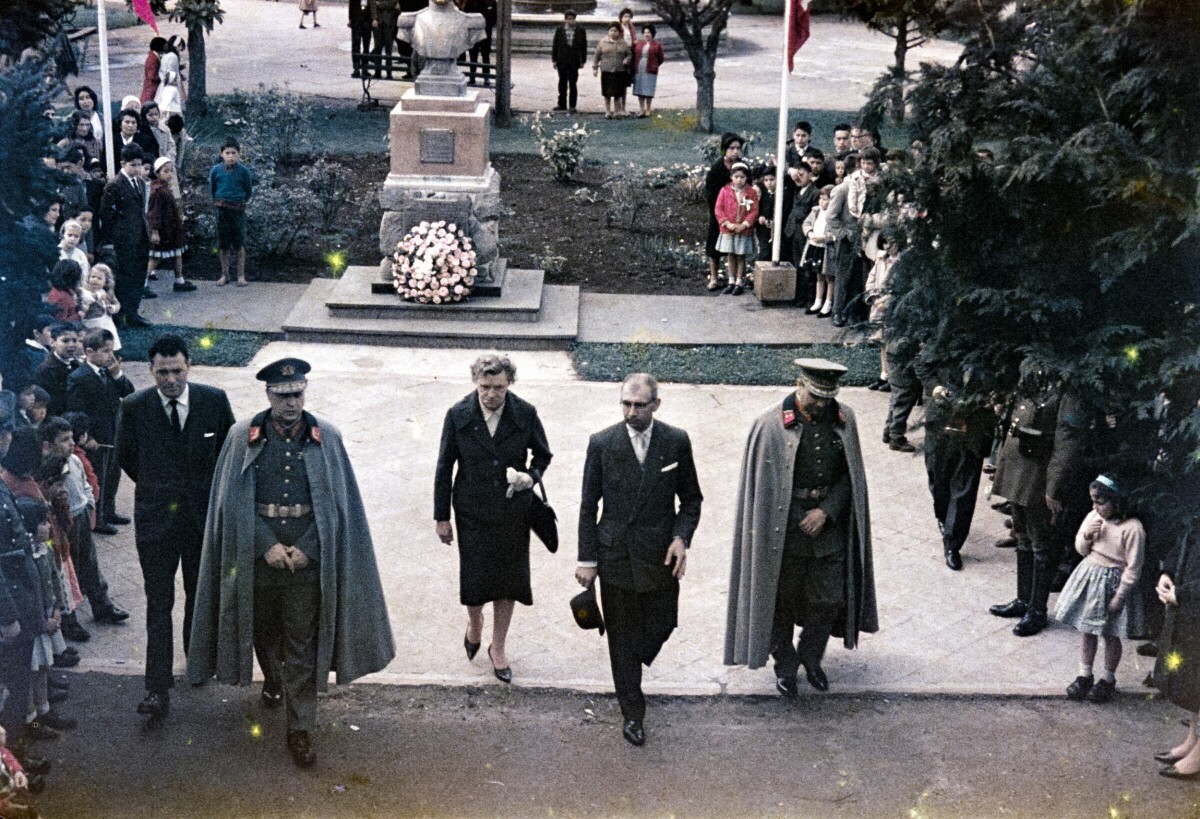 Plano entero de Gobernadora Olga Boettcher junto a 2 militares y dos hombres con Traje caminando frente a estatua de Bernardo O'higgins en plaza de la Concordia de La Unión