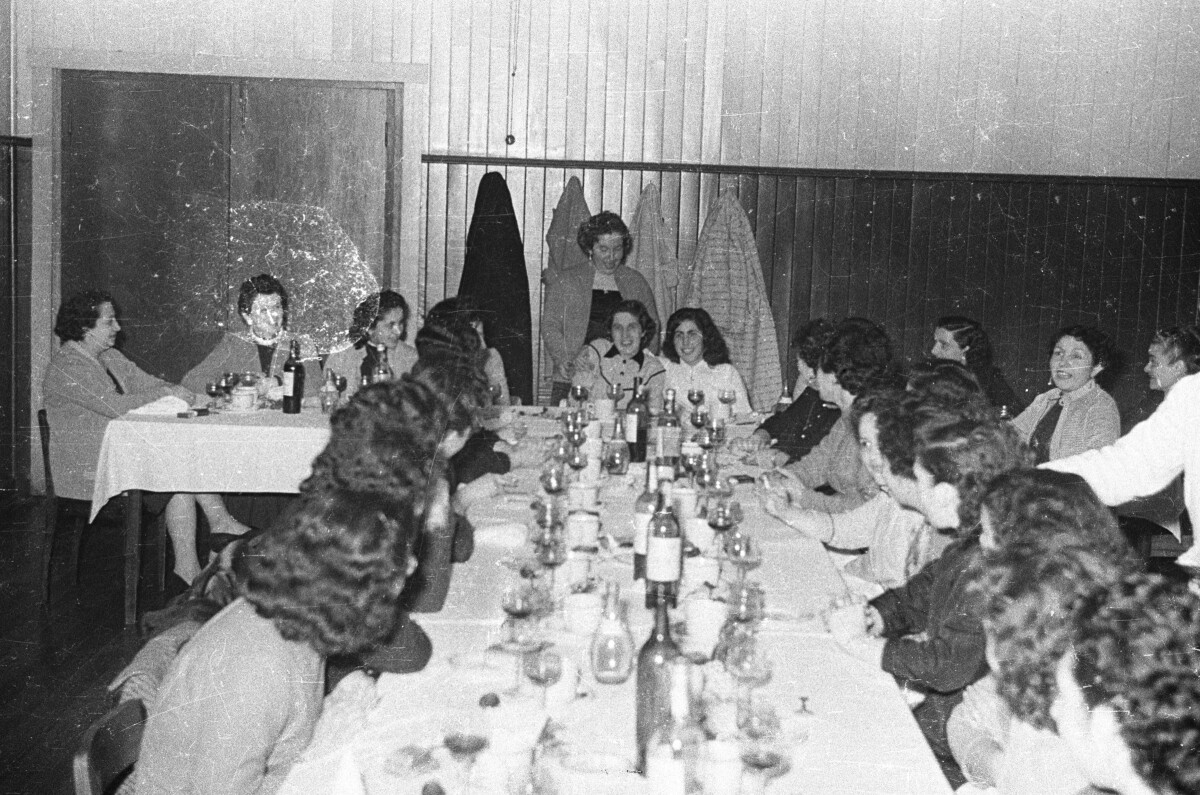 plano general de un grupo de mujeres riendo y conversando, sentadas alrededor de una mesa, durante un banquete en el interior de una estructura no identificada