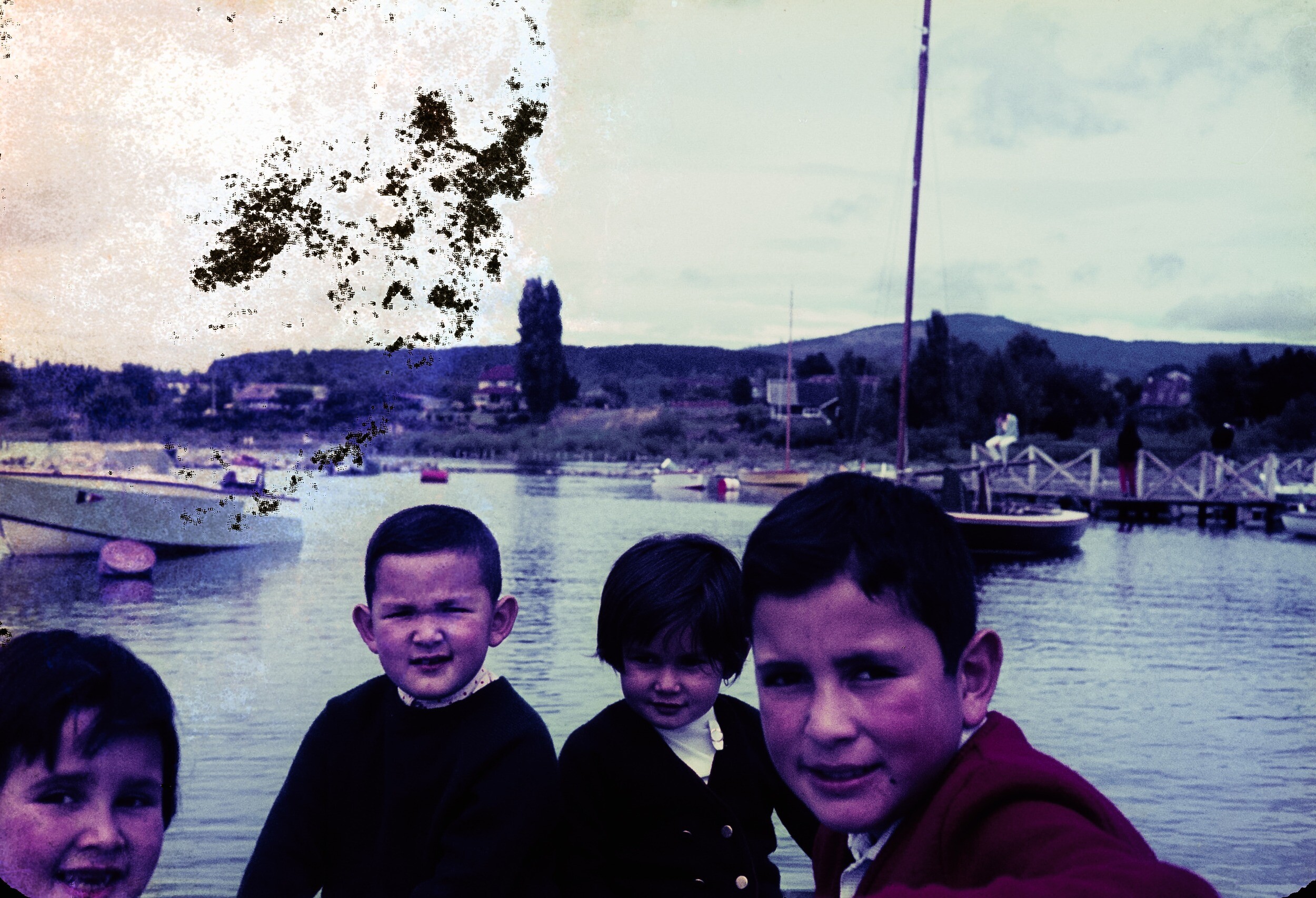 Retrato de plano medio de dos niños y dos niñas posando de frente detrás de ellos un lago con botes y un muelle