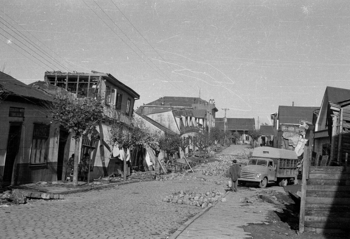 Plano general de dos hombres y mujer en las afueras de casas apuntaladas y escombros producto del terremoto del 60' en la ciudad de Valdivia