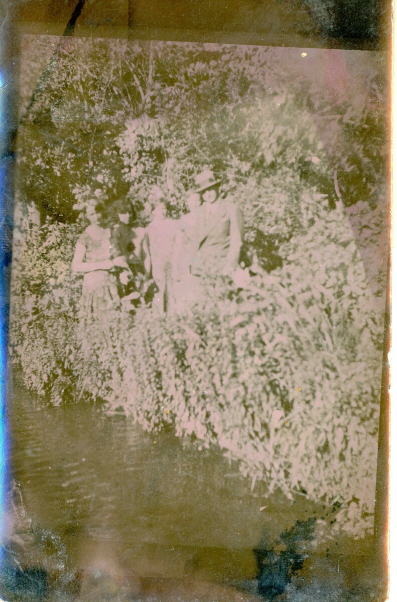 Retrato de plano entero de un hombre y un grupo de mujeres posando entre los arbustos junto a un RÍO no identificado.