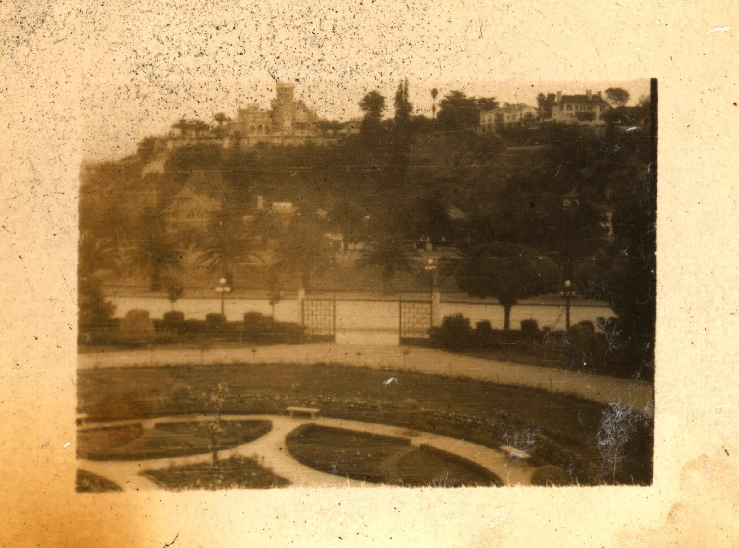 Vista general desde el interior de una plaza enrejada. Al frente, un cerro con edificaciones en su cima.