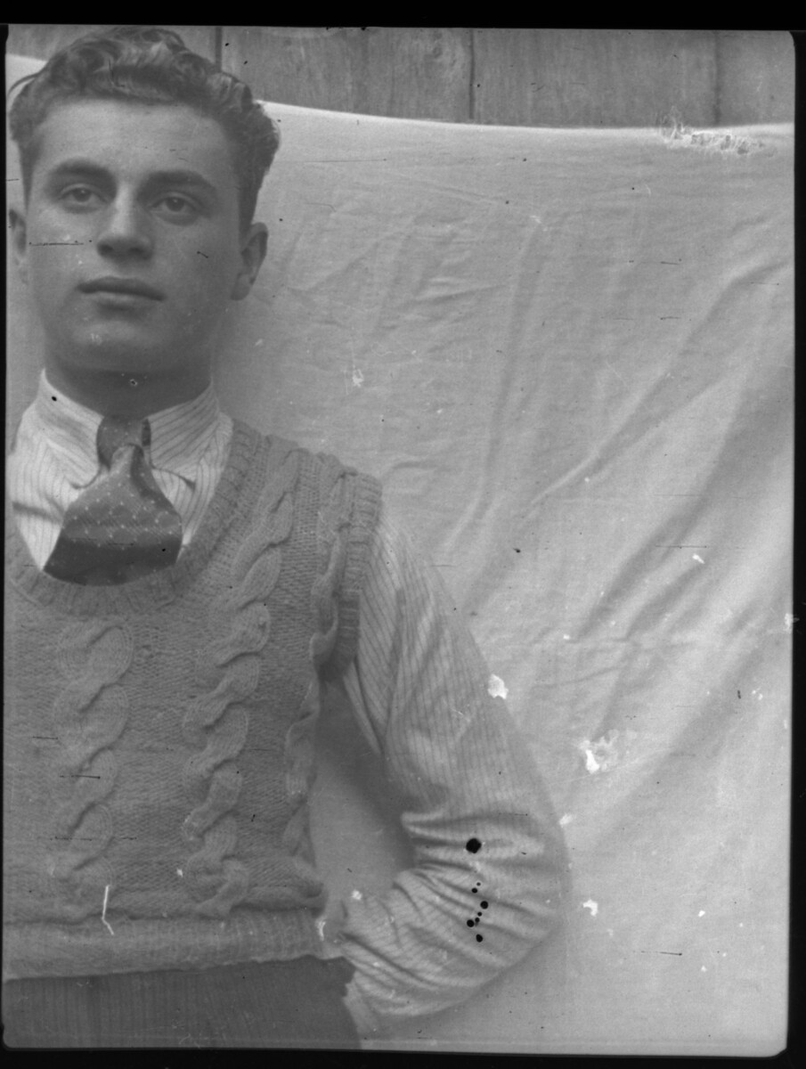 Plano medio de un hombre joven, posando de pie delante de un lienzo de tela colgado al muro