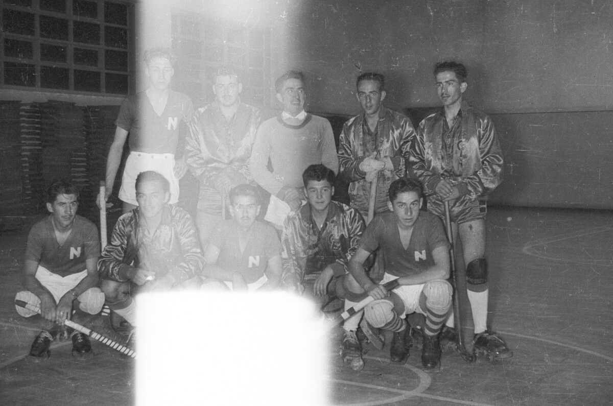Retrato grupal de plano entero de un equipo de hokey masculino no identificado, formado en el interior de la cancha de un gimnasio
