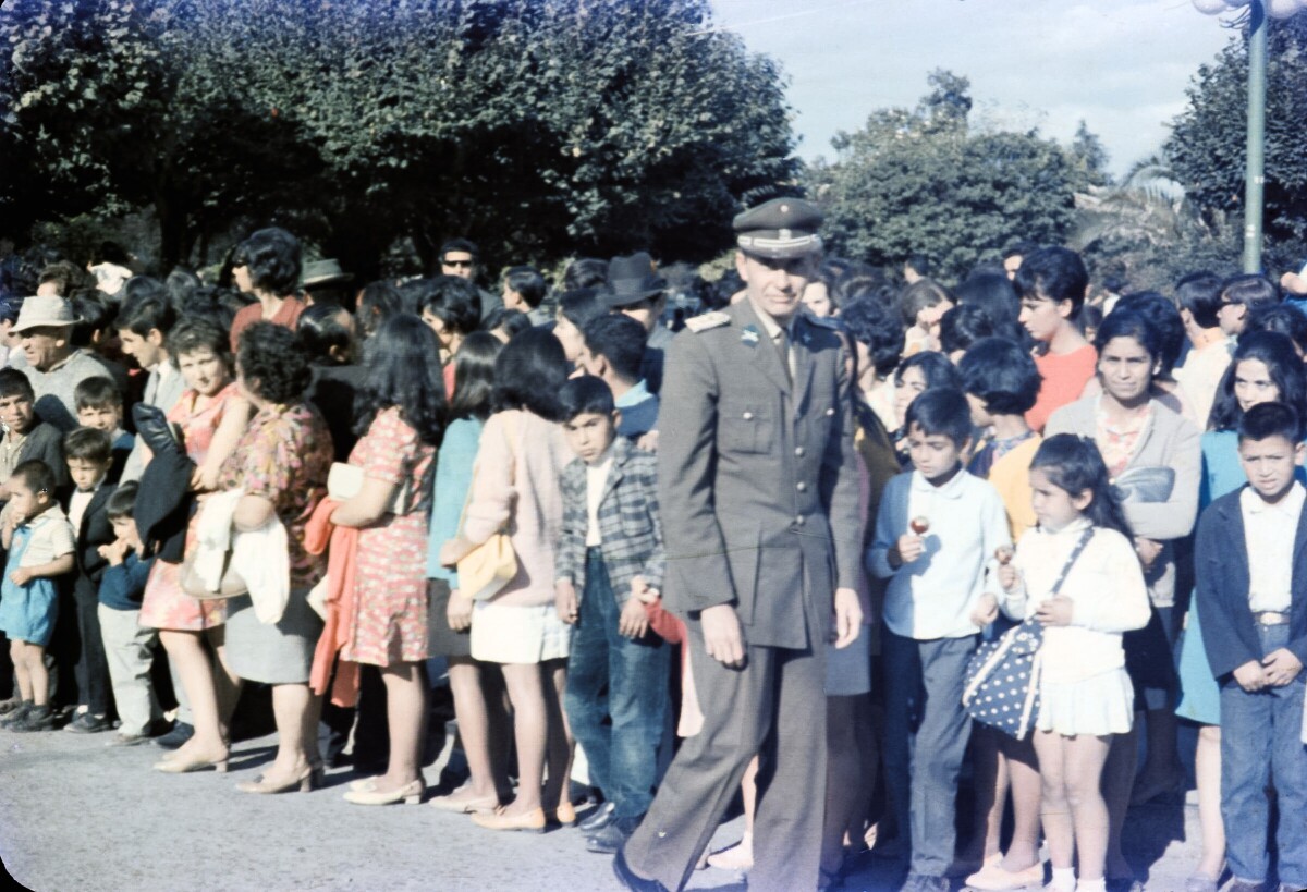 Retrato de plano entero de Carabinero caminando frente a un grupo de personas agrupadas al borde de una calle en Plaza de la Concordia de La Unión