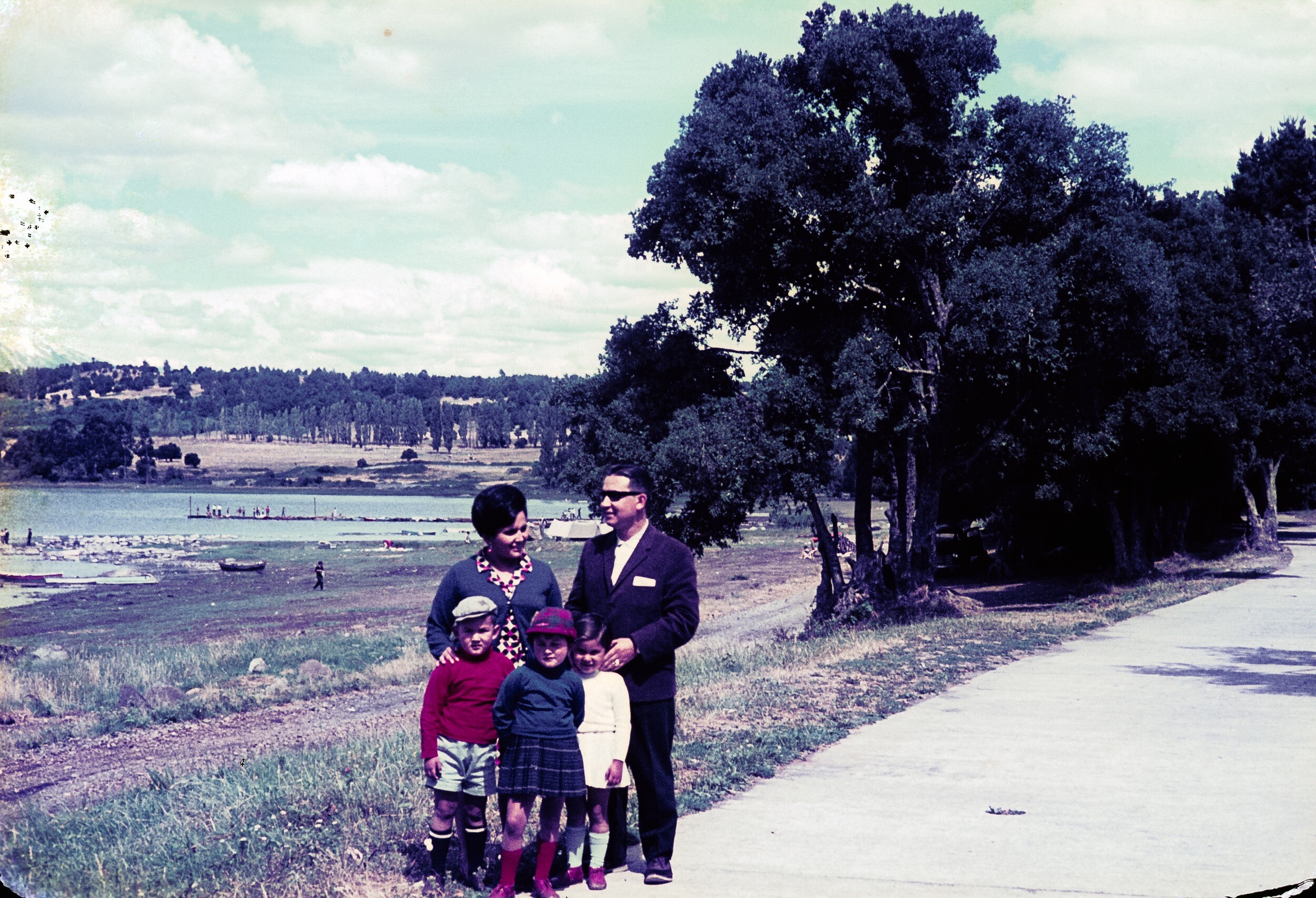 Retrato de plano entero de Hombre con Traje, Mujer con Chaleco, dos niñas y un niño a orilla de un camino al borde de un prado con árboles