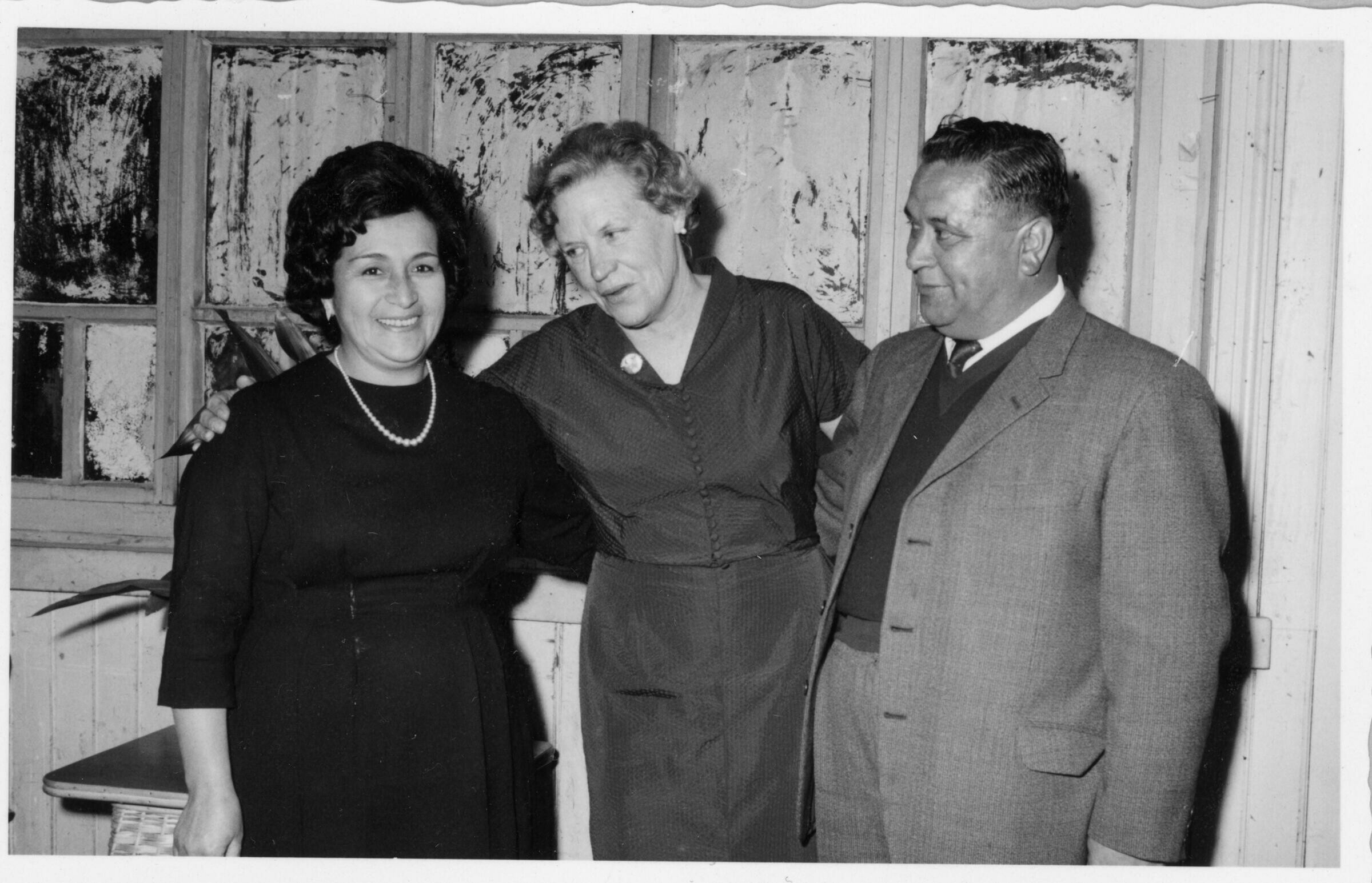 Retrato de plano medio largo  de Olga Boettcher posando junto a una mujer y un hombre. Se encuentran ubicados junto a una ventana, en el interior de un local no identificado durante  un banquete realizado en su honor, tras haber finalizado su gobernación