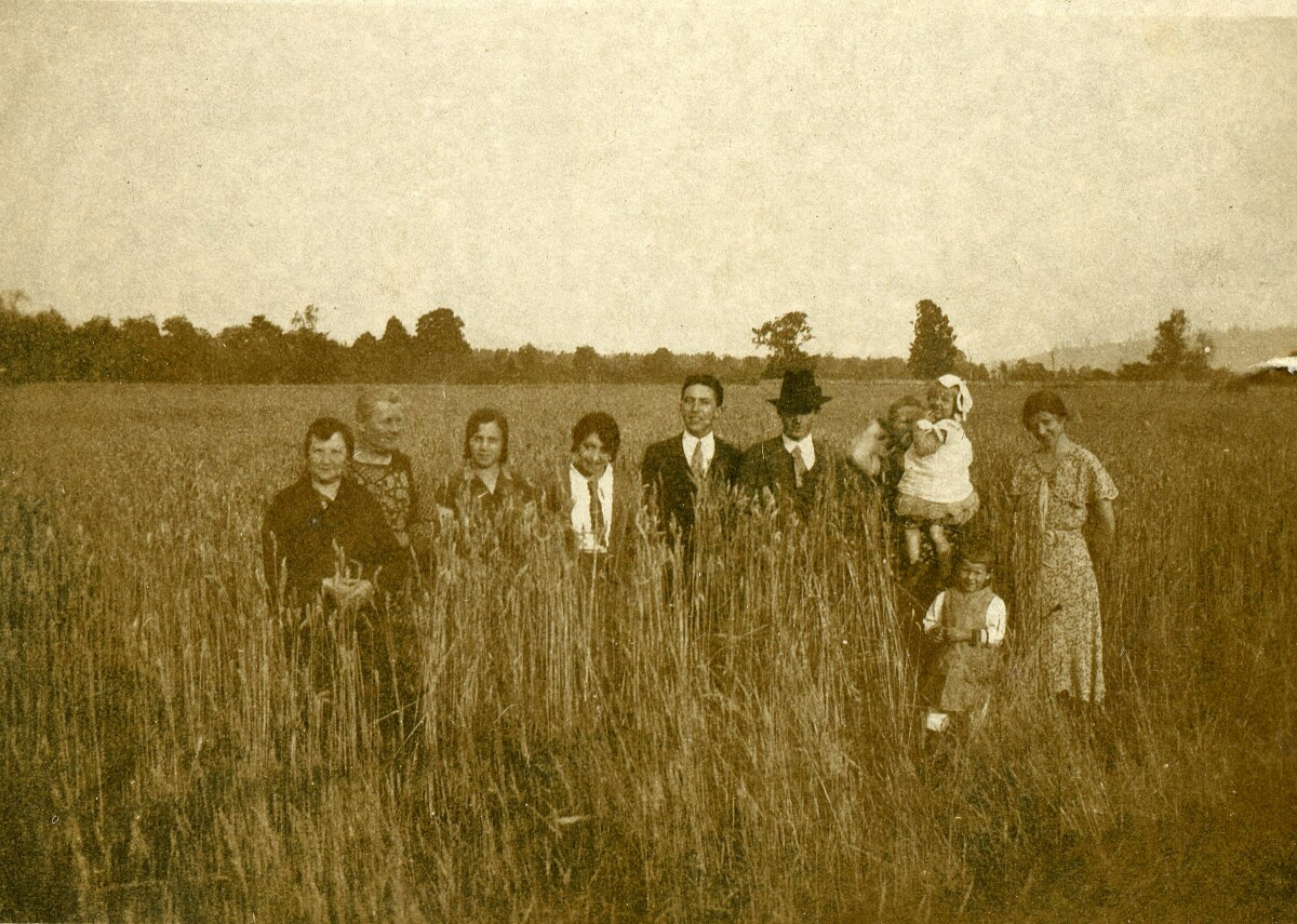 Retrato grupal de plano entero de Mujeres, Hombres y dos niñas posando parados en el medio de un campo de trigo.