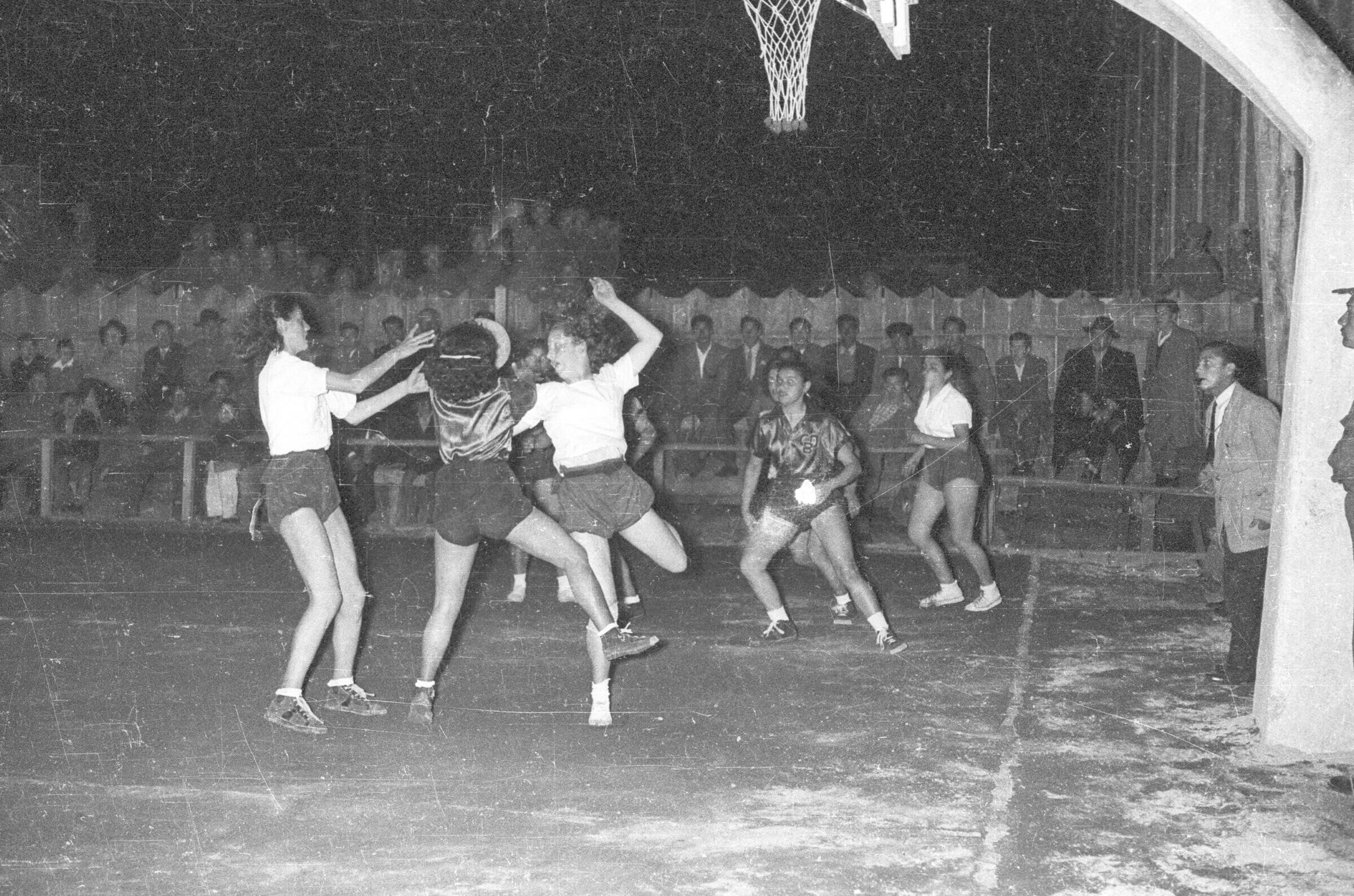 plano general de dos equipos de baloncesto femenino disputando el balón en el interior de la cancha durante un partido realizado durante la noche