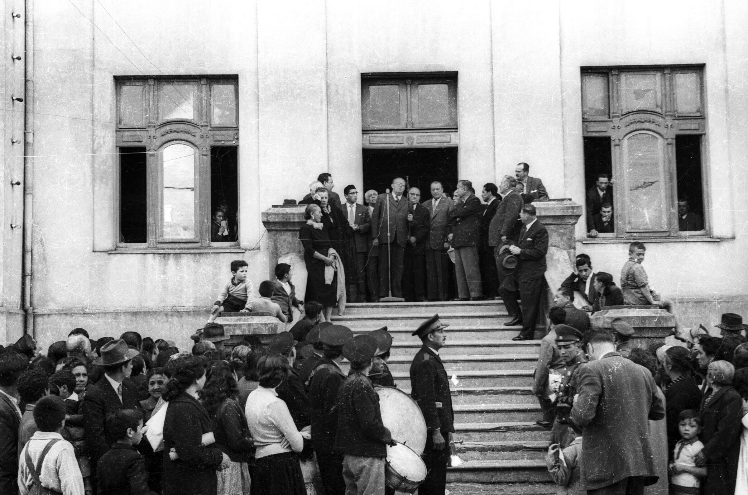 plano general de un grupo numeroso de personas reunidas en la vereda mientras que Carlos Vogel da un discurso en el frontis de la municipalidad
