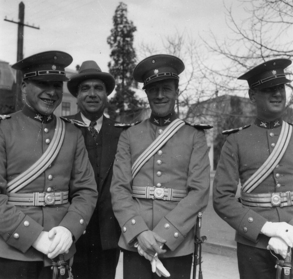 Retrato de plano entero de un hombre de Traje, posando en el medio junto a dos uniformados de carabineros. Todos sonríen. En el medio se encuentra ubicado el Capitán Núñez. Al costado derecho hay un tercer carabinero quien está mirando hacia un costado. Se encuentran parados en la calle, ubicados a un costado de la plaza de La Concordia