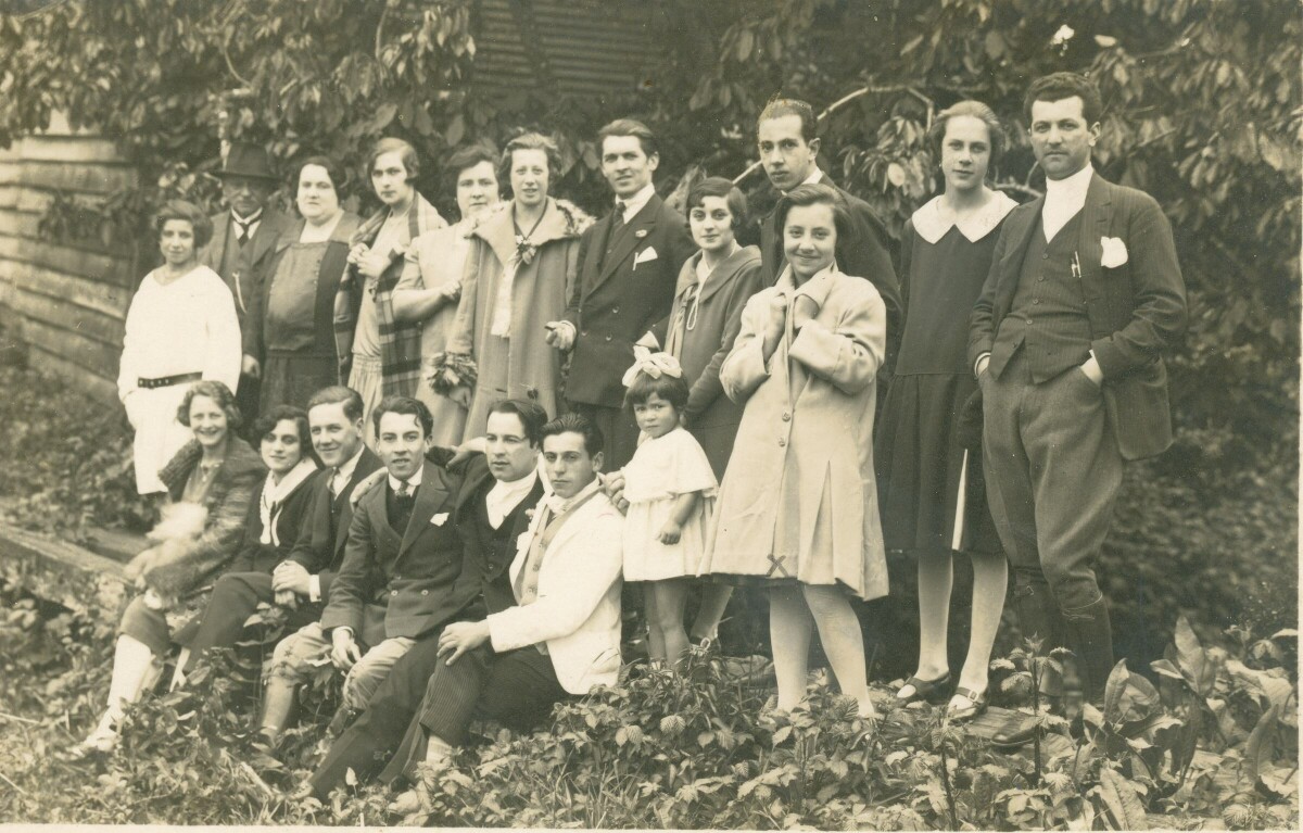 Retrato grupal de plano entero de hombres, mujeres y una niña posando en el jardín de una casa.