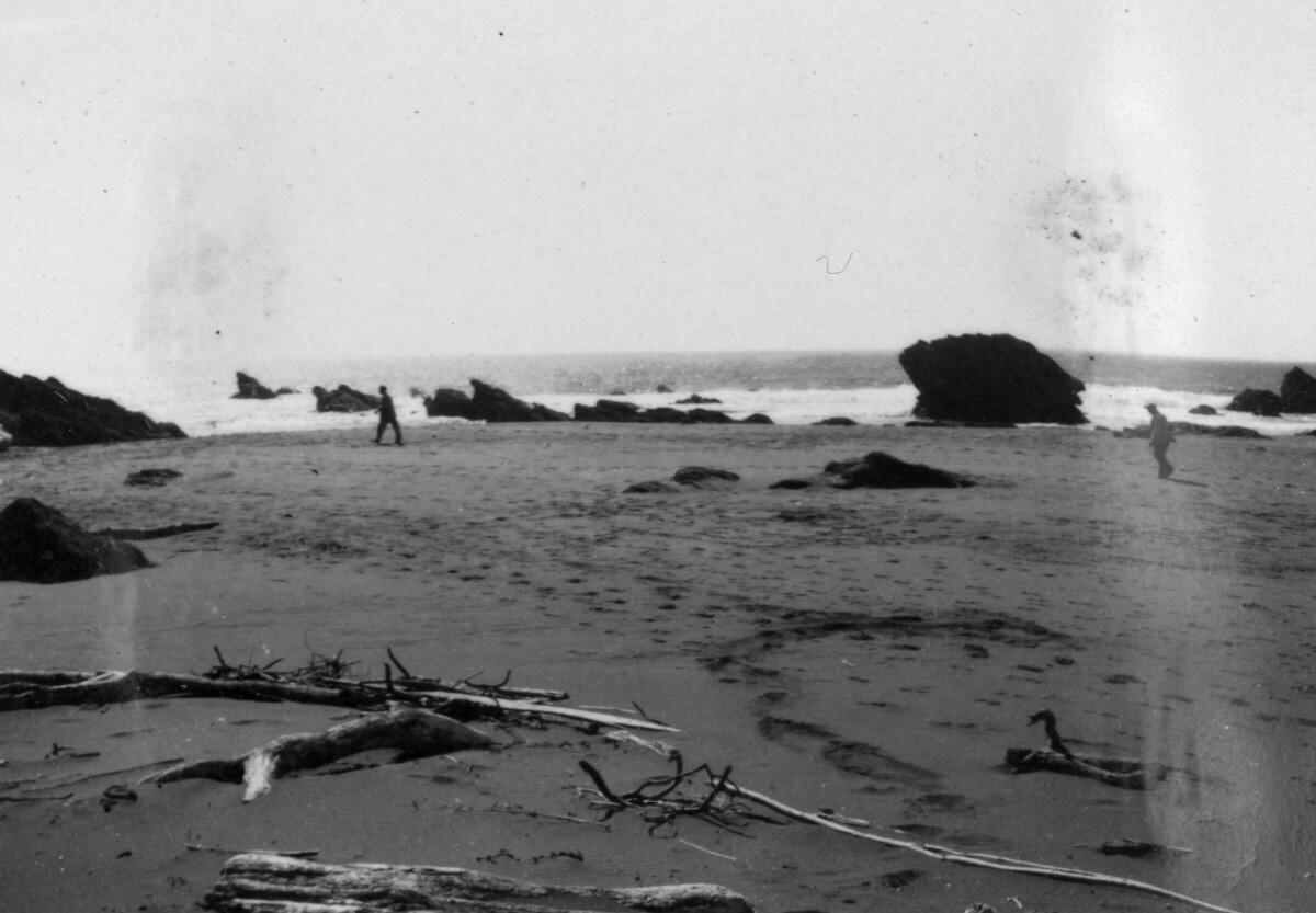 plano general de una playa. Sobre la arena van dos hombres caminando a metros de distancia entre sí. En la costa existe un roquerío. La fotografía fue tomada durante un paseo al balneario de Hueicolla