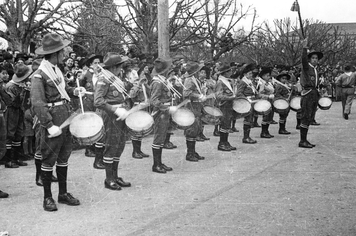 plano general del tambor mayor dirigiendo la banda mientras levanta una guaripola, tras él hay un grupo de niños vestidos con sus uniformes, tocando sus instrumentos durante un desfile en la ciudad de la Unión