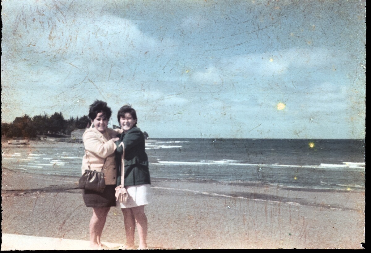 Retrato de plano entero de dos mujeres con Vestido abrazadas a orilla de una playa