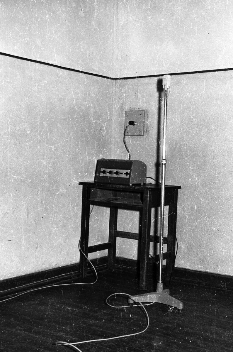 Plano entero de un micrófono de pie junto a amplificador encima de un pupitre