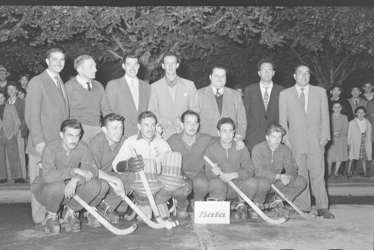 Retrato grupal de siete hombres vestidos con traje junto a seis jugadores de hockey posando, los jugadores tienen en sus manos un palo de hockey.