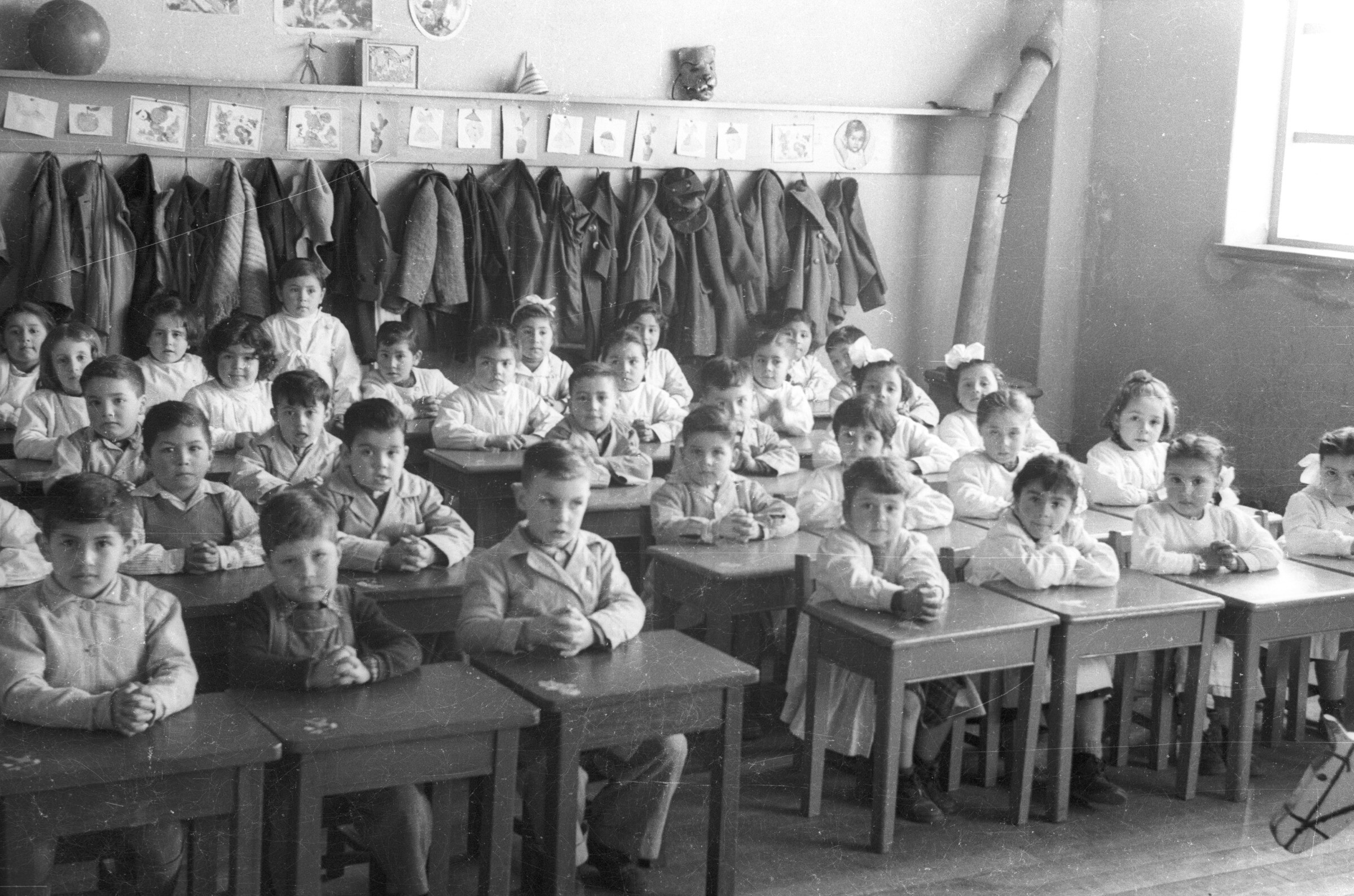 Retrato grupal de plano entero de grupo de Niños y niñas con delantal sentados en sus pupitres en una sala de clases