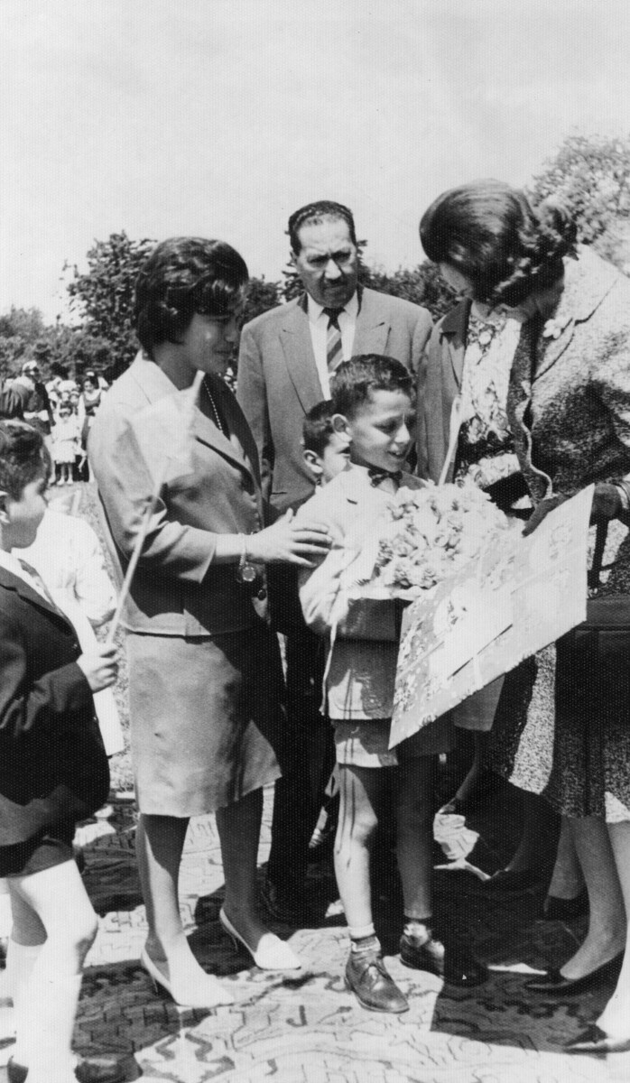 Plano entero de Eva Sámano de López Mateos, primera dama de México, entregándole un presente a un Niño. Los acompañan una mujer, dos niños y un hombre vestido de Traje. Se encuentran en el interior de un recinto no identificado, durante su visita a La Unión