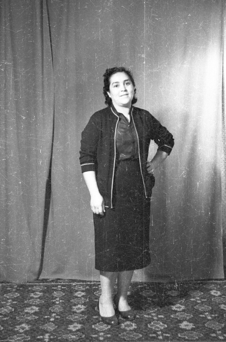 Retrato de estudio de plano entero de una mujer posando con una mano en la cadera, parada sobre una alfombra