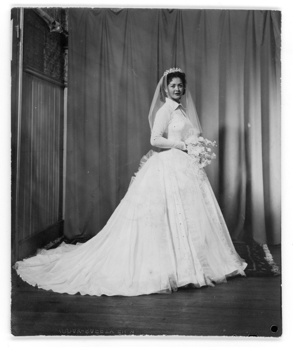 Retrato de estudio de Plano entero de una mujer vestida de novia, posando con un ramo de flores y la cola de su vestido hacia un costado