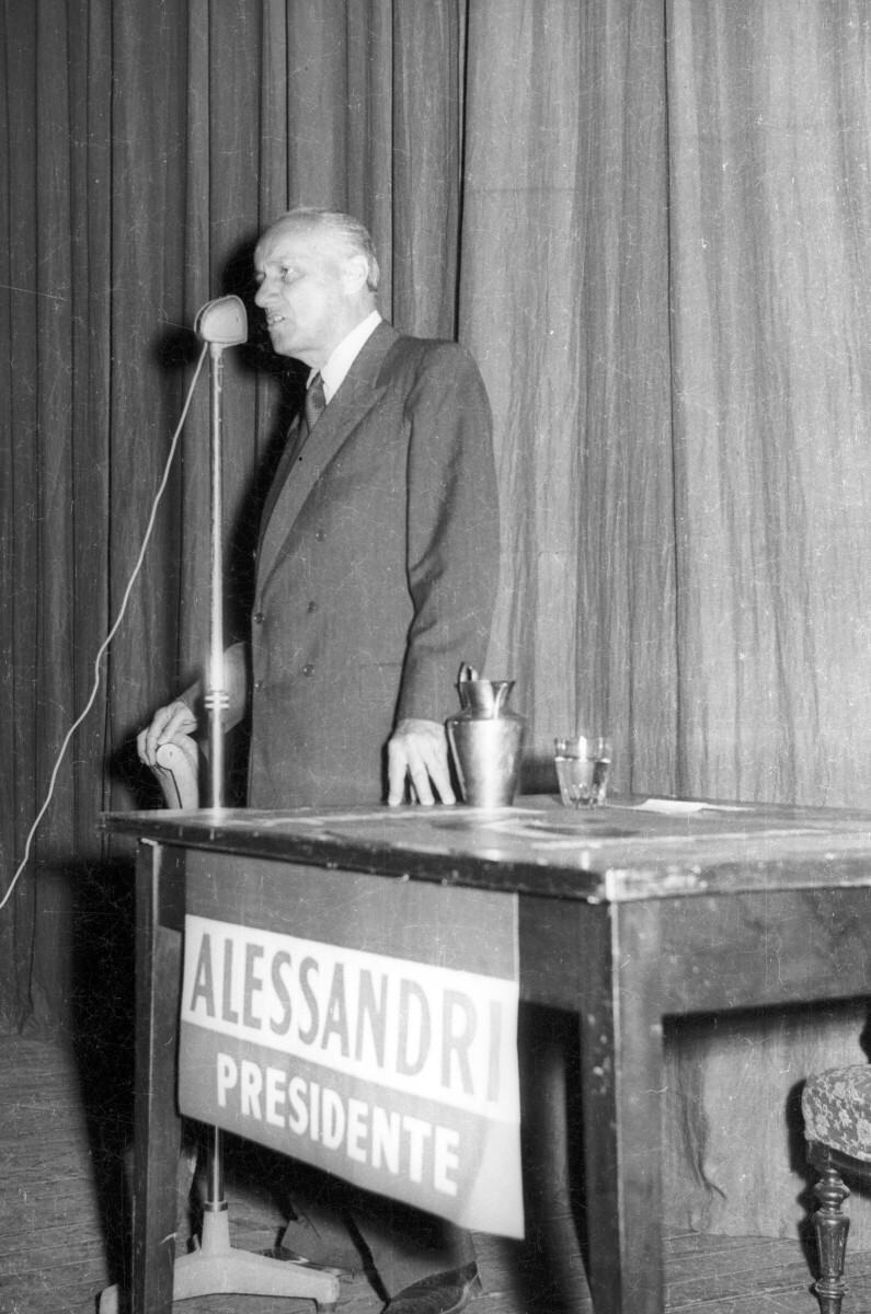 plano general de Jorge Alessandri hablando por un micrófono durante su campaña presidencial. Se encuentra de visita en la ciudad de La Unión.