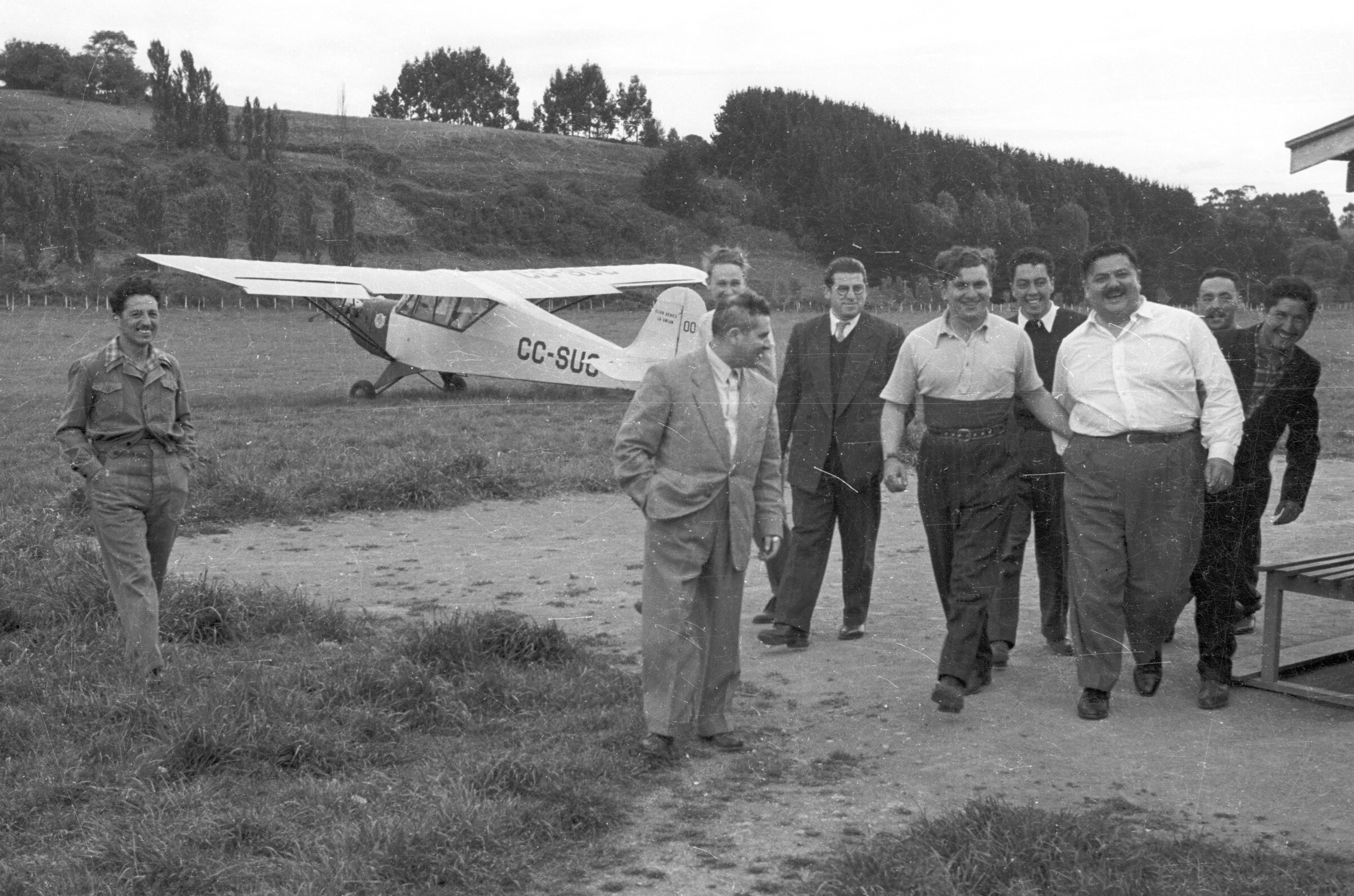 Plano entero de un grupo de hombres caminando junto al nuevo integrante a quien lo dirigen a un costado de una casa para llevar a cabo su iniciación del club aéreo de La Unión