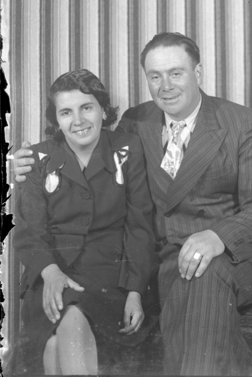 Plano medio largo de una pareja sonriendo y posando sentadas para un retrato en un estudio fotográfico