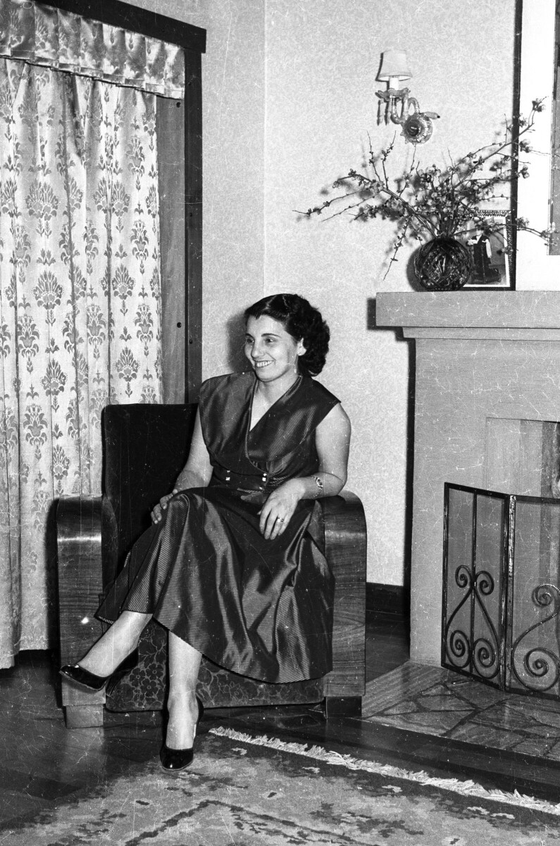 Retrato de plano entero de Jovita Navarrete de Lopetegui, sonriendo mientras posa con las piernas cruzadas en un sillón. Se encuentra en el interior de una casa